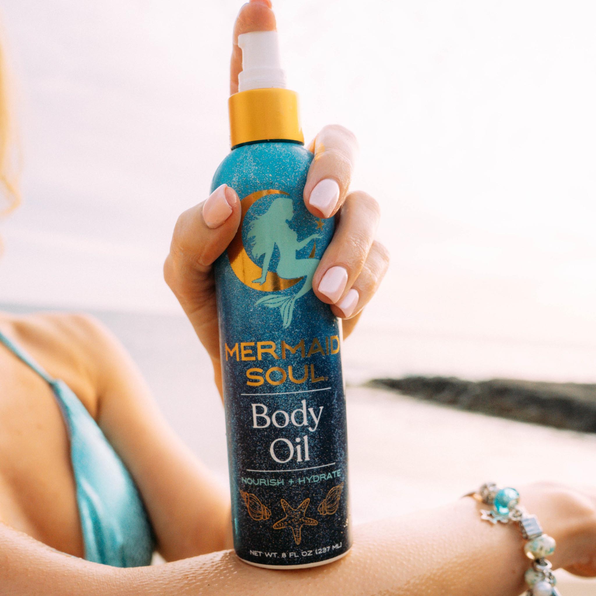 Person applying Mermaid Soul body oil to their arm with a beach background