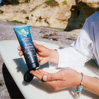 Person holding a tube of Mermaid Soul Body Butter by a body of water.