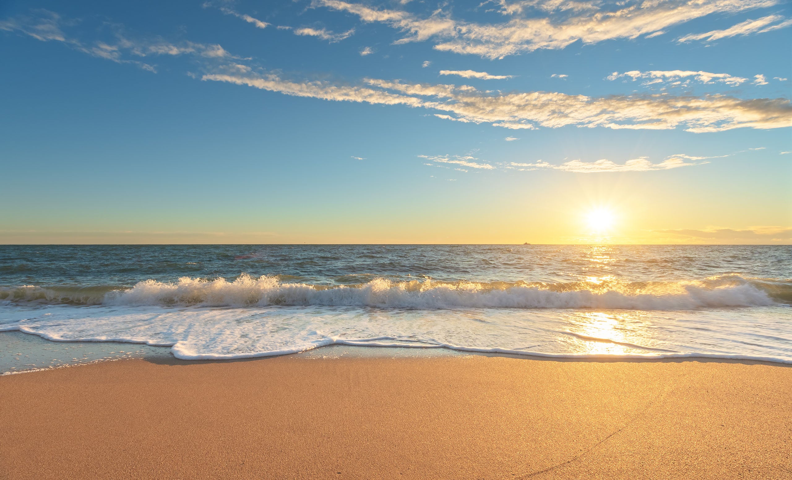 Sunset over the ocean with waves crashing onto a sandy beach.